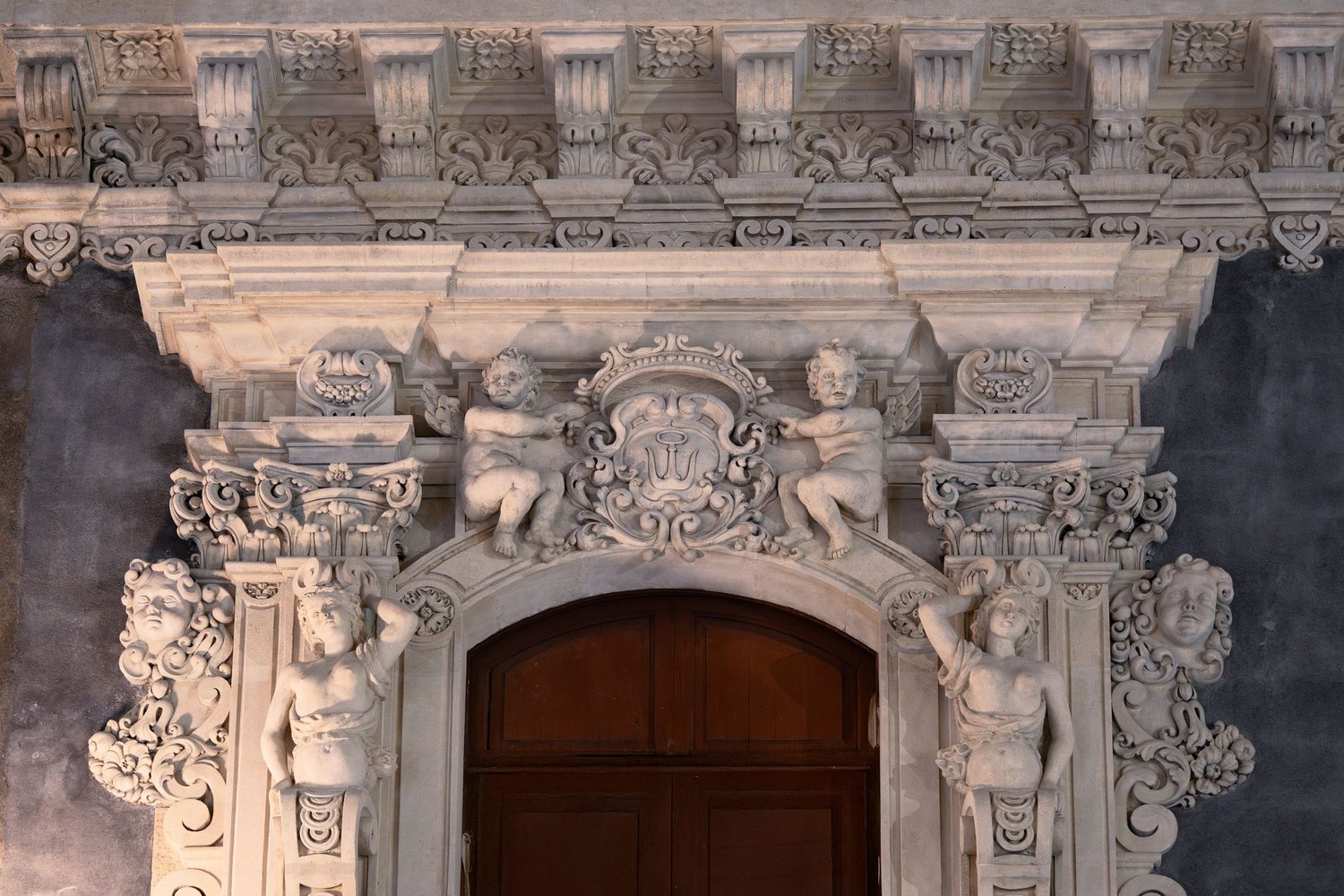Catania, Palazzo San Demetrio in via Etnea, portale tardobarocco con putti, telamoni e stemma.