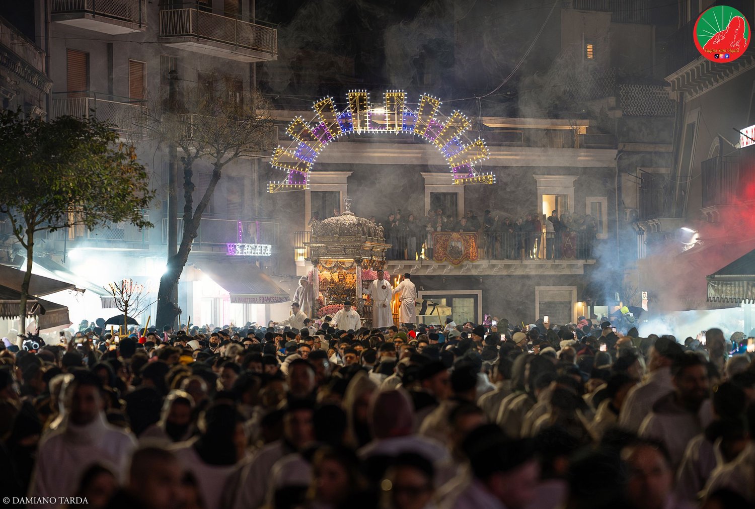 Folla di devoti di notte durante la festa di Sant'Agata, con le luminarie sullo sfondo.